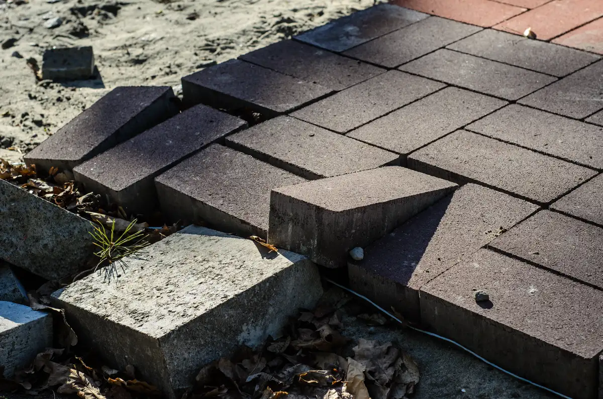 Fragment chodnika z betonowych kostek z podniesionymi płytkami podczas wymiany kostki brukowej