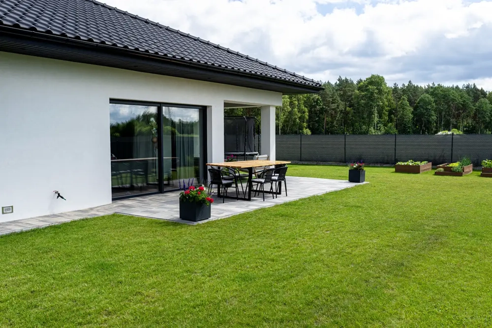 Płyty tarasowe betonowe na patio przy domu z trawnikiem z rolki