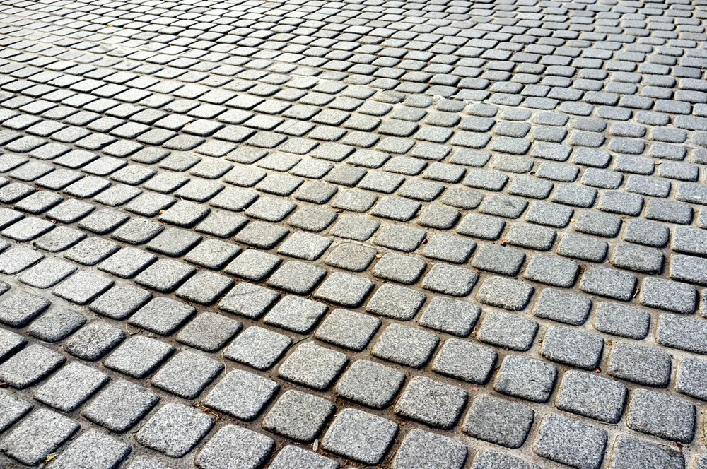 Układanie kostki brukowej z szarych kwadratowych elementów tworzących równą nawierzchnię