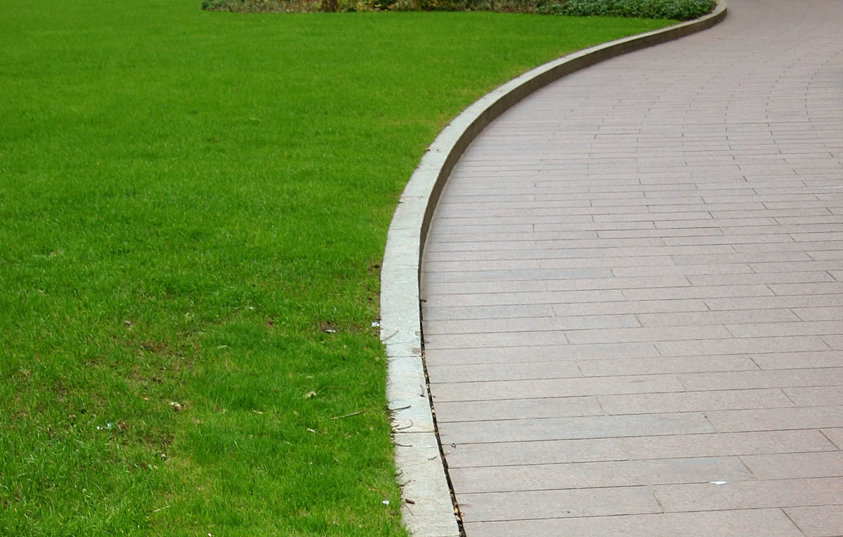 Zakrzywiony chodnik betonowy z betonowym krawężnikiem przy zielonym trawniku