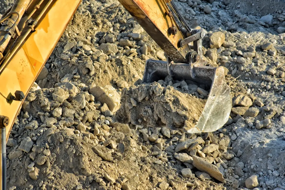 Koparka podczas prac ziemnych z łyżką pełną ziemi i kamieni