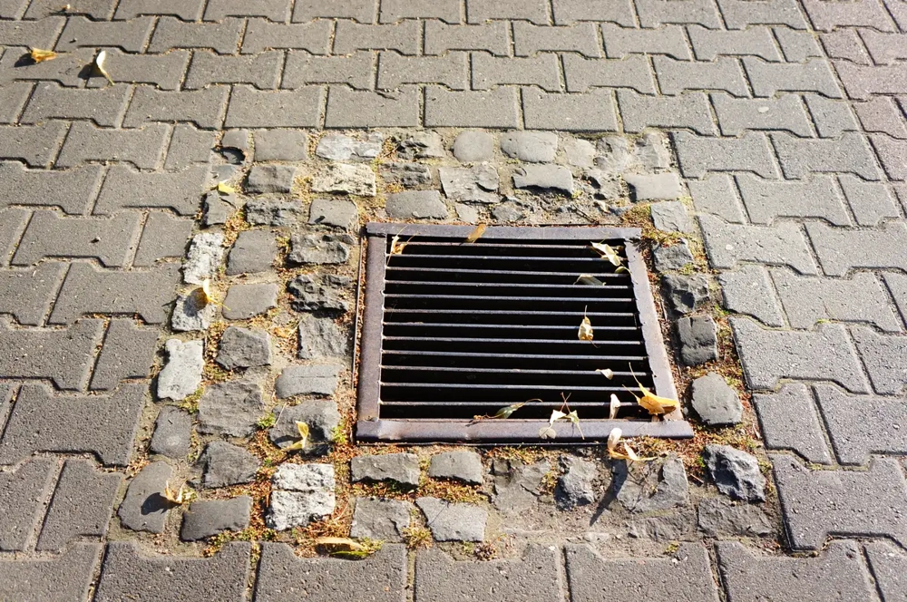 Kratka ściekowa osadzona w kamiennym obrzeżu i kostce brukowej na chodniku – odwodnienia liniowe
