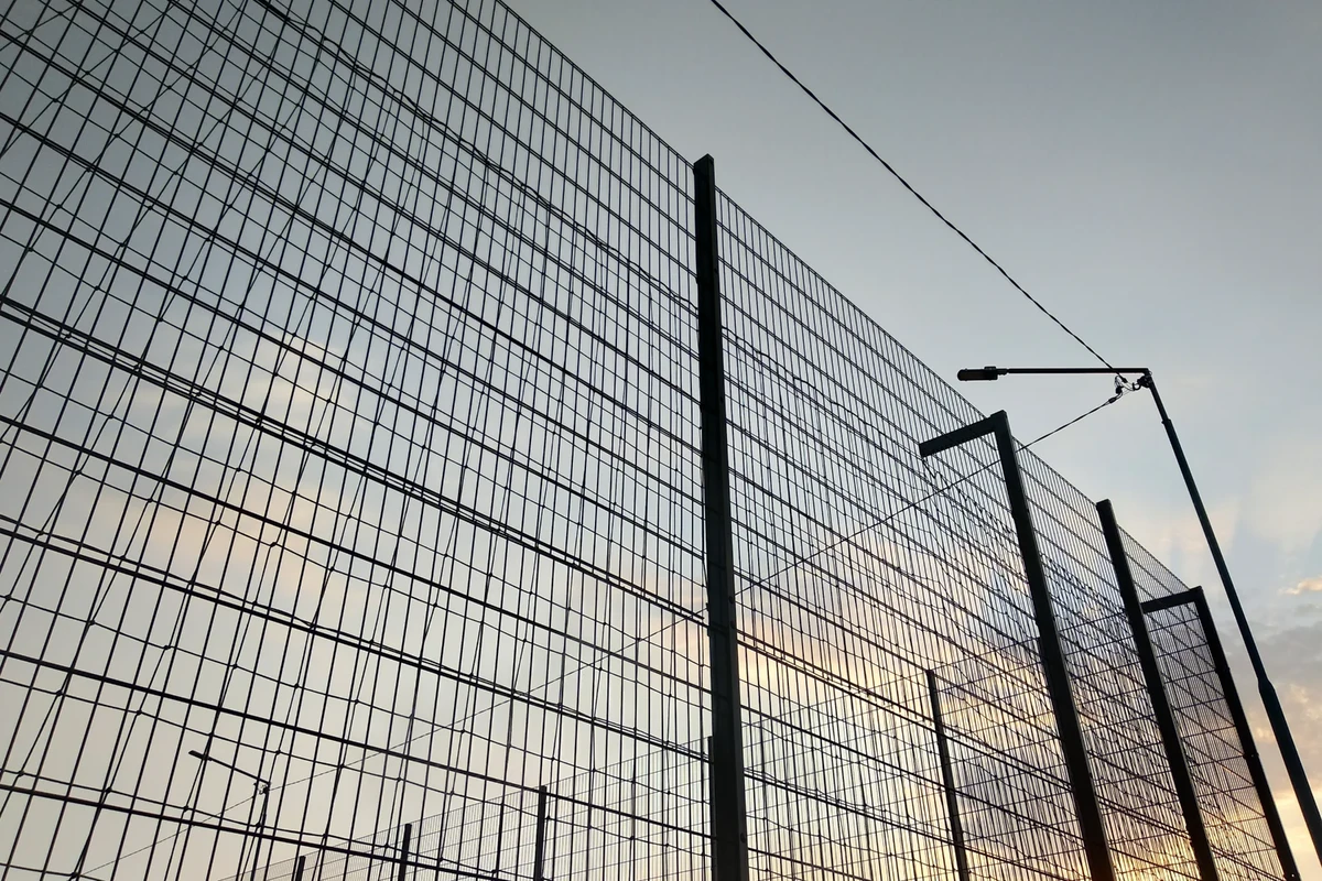 Ogrodzenia panelowe z siatki stalowej zamontowane na metalowych słupkach na tle zachodzącego nieba